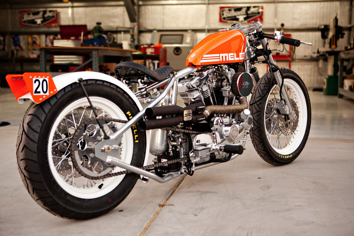 A photo of the bike angled from the back tire showing the bike's orange paint, race number, and white tires with chrome